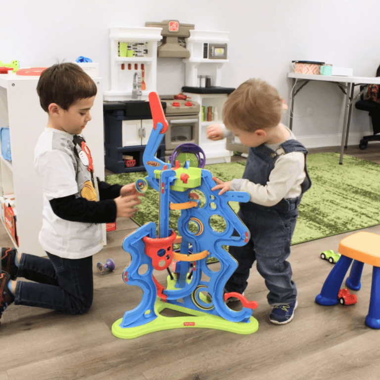 Two young children playing with a colorful marble run toy in a therapy room, promoting social interaction and developmental support.